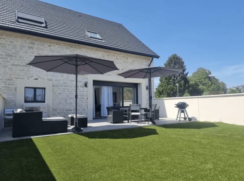 Terrasse en pierre du gîte Les Camélias 71 à Oslon avec parasols noirs, espace repas et pelouse soignée