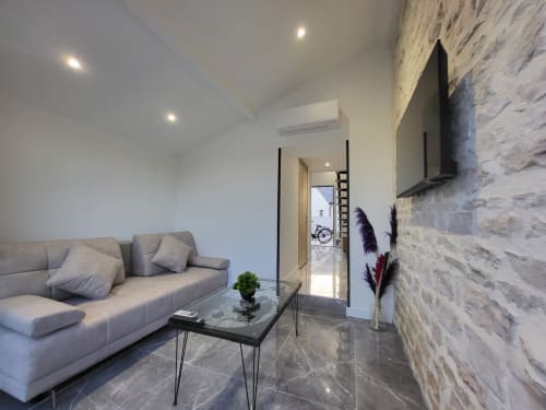 Salon moderne aux Gîtes Les Camélias 71 à Oslon, France avec canapé gris et mur en pierre