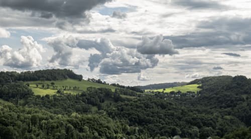 Collines verdoyantes et forêts denses près des Gites Les Camelias 71 à Oslon, France, sous un ciel nuageux dramatique