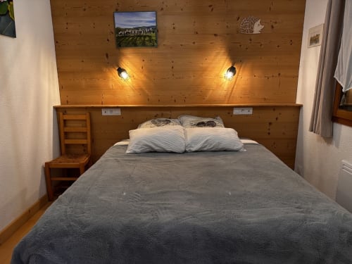 Chambre douillette du gîte Des Planchettes à Marigny avec tête de lit en bois, éclairage chaleureux et literie grise