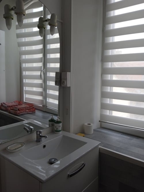 Salle de bains moderne avec vasque blanche, stores à rayures et équipements sanitaires à l'hôtel Varette Patricia, Saint-Floxel