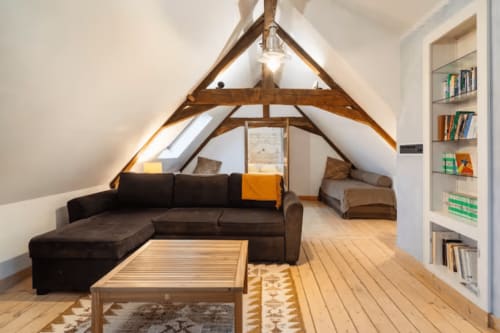 Chambre mansardée à la Villa République Normandie à Caen avec canapé sombre, poutres en bois, bibliothèques et puits de lumière