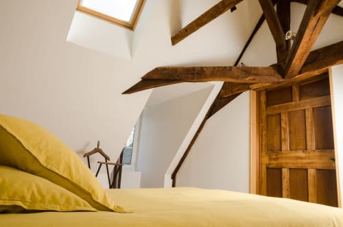 Chambre lumineuse aux draps jaunes, poutres apparentes, verrière et armoire en bois à la Villa République Normandie de Caen