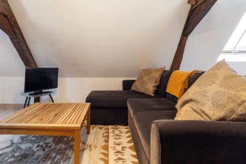 Salon cosy au grenier de la Villa République Normandie à Caen avec poutres apparentes, canapé gris anthracite et table en bois