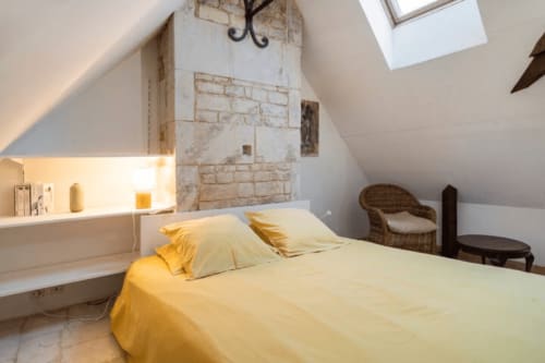 Chambre lumineuse sous les toits à la Villa République Normandie de Caen, avec linge de lit jaune, pierre apparente, velux et fauteuil en osier