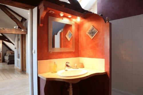 Alcôve de salle de bain aux tons orange vibrants avec lavabo et miroir illuminés à la Villa République Normandie, Caen