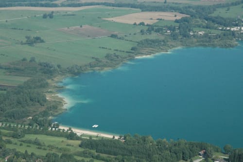 Vue aérienne du lac turquoise avec prairies verdoyantes et rives boisées près des Gîtes Des Planchettes, Marigny