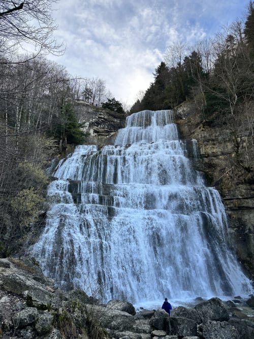 Cascade gelée sur terrain rocheux près de Marigny, France, avec sapins et branches nues en hiver