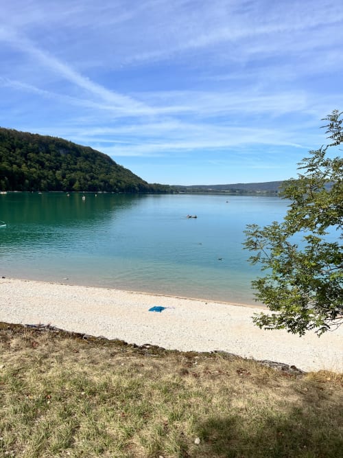 Plage au lac turquoise avec collines boisées et bateaux, Gîtes Des Planchettes, Marigny
