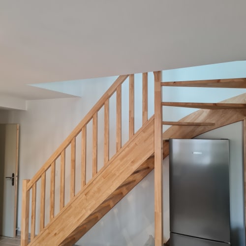 Escalier en bois moderne avec rampe dans un gîte rustique, réfrigérateur inox visible au Gîte Les Mouettes Blessées