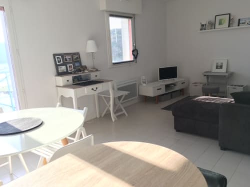 Intérieur lumineux d'appartement avec coin repas, bureau, télévision, canapé noir et vue sur la mer à Belle Île en Mer