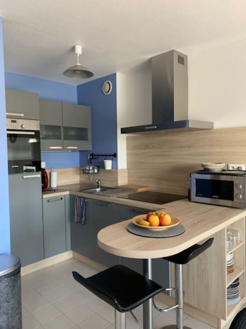 Cuisine moderne aux murs bleus, plan de travail en bois, îlot de repas et électroménagers inox à Belle Île en Mer