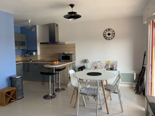 Cuisine ouverte et élégante avec table ronde blanche, détails en bois et accès à la vue mer