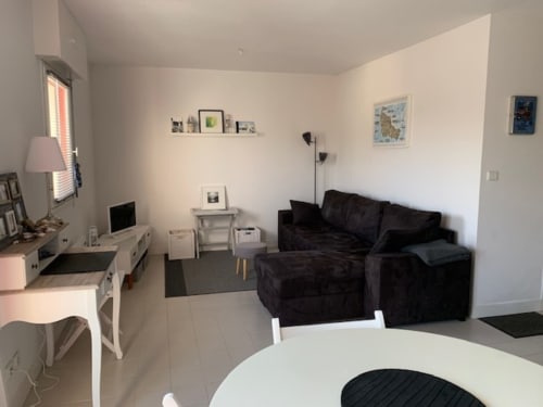 Appartement moderne à Loc'Maria Belle Île avec canapé noir, table à manger blanche, espace de travail et œuvre d'art vue sur mer