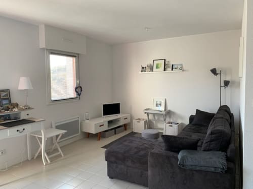 Salon lumineux à Locmaria avec canapé noir, téléviseur, bureau et vue sur la mer