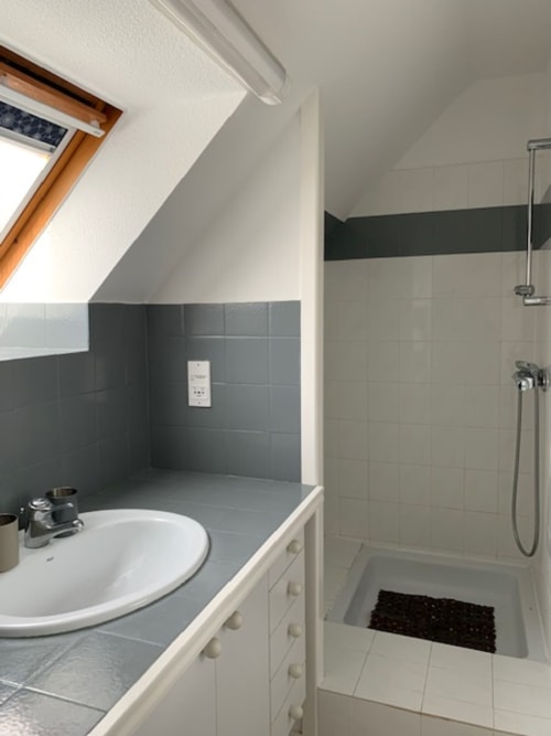 Salle de bain moderne de l'appartement Belle Île en Mer avec lavabo, douche, carrelage foncé et plafond en pente avec lucarne