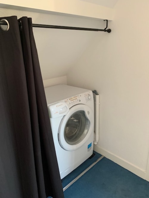 Lave-linge blanc dans un coin buanderie avec tringle et rideau noirs, Belle Île en Mer
