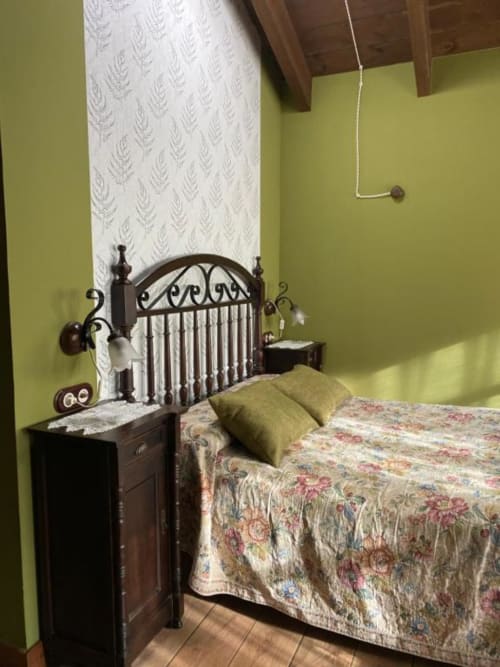 Dormitorio del Hotel Rural Los Texos con cama de hierro forjado, paredes verde lima, ropa de cama floral y vigas de madera en el techo