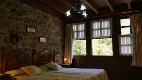 Dormitorio rústico con cama de madera, muros de piedra y amplios ventanales con vistas al jardín en Hotel Rural Los Texos