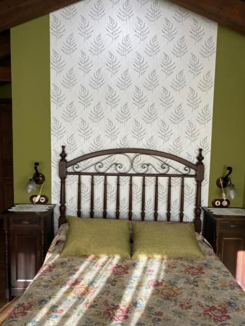 Acogedora habitación en Hotel Rural Los Texos con cama metálica ornamental, cabecero con estampado de helechos, almohadas verdes y ropa de cama floral.