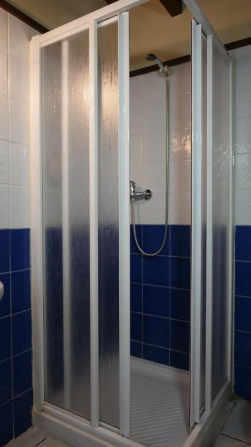 Cabina de ducha con puertas de cristal esmerilado y marco blanco en el baño del Hotel Rural Los Texos, paredes azul marino