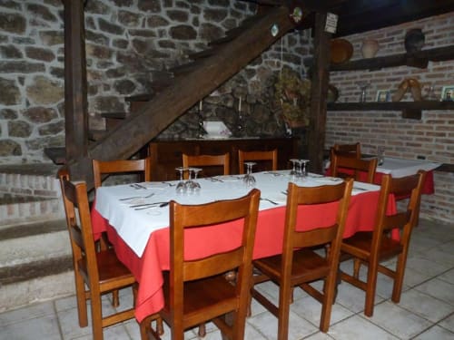 Comedor rústico del Hotel Rural Los Texos con sillas de madera, manteles rojos, muros de piedra y vigas de madera vista.