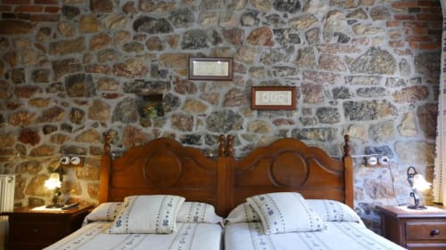Dormitorio rústico de piedra en Hotel Rural Los Texos con camas de madera, sábanas blancas y vista al jardín en Covadonga
