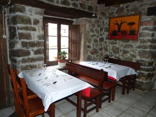 Rústico comedor de piedra en Hotel Rural Los Texos con mesas vestidas de blanco, sillas de madera y arte africano