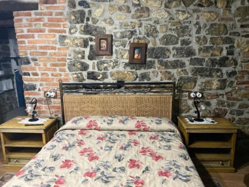 Dormitorio rústico en Hotel Rural Los Texos con paredes de piedra, ropa de cama floral y mesillas de madera