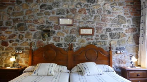 Habitación rústica de piedra en Hotel Rural Los Texos con cama de madera, ropa blanca y encantadora vista al jardín
