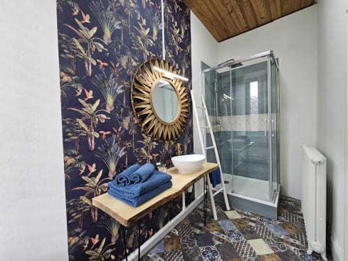 Salle de bain moderne à la Bastide du Thoré avec papier peint botanique, miroir soleil doré, vasque blanche et douche vitrée
