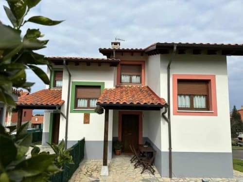 Charming white villa with terracotta tile roof and colorful window frames in Ribadesella, Spain