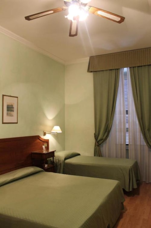Camera tripla dell'Hotel Fiori Roma con due letti, testiere in legno, pareti verdi e vista sulla città dalla finestra con tende