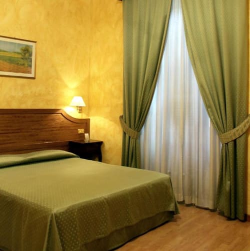 Camera doppia all'Hotel Fiori di Roma con due letti singoli, pareti gialle, tende verdi, testata in legno e vista sulla città dalla finestra