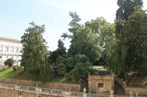 Giardino dello storico Hotel Fiori a Roma con lussureggiante verde, terrazza in pietra e architettura classica che si affaccia sulla città