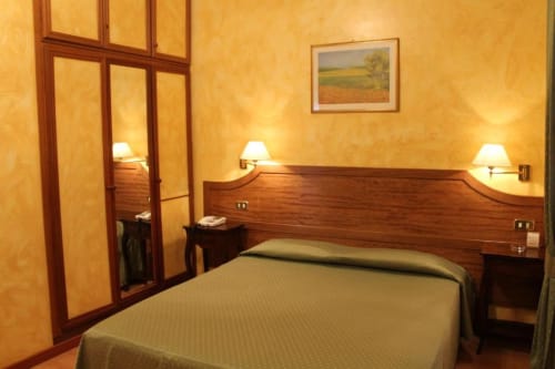 Camera doppia Hotel Fiori Roma con testata in legno, letti gemelli, pareti gialle, lampade da comodino e armadio a specchio