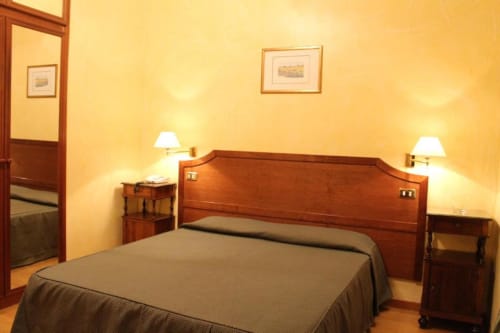 Elegante camera doppia all'Hotel Fiori Roma con letto in legno, lampade comodino, pareti gialle e pavimentazione in parquet