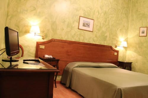 Camera doppia all'Hotel Fiori di Roma con letti gemelli, testata in legno, scrivania con TV, illuminazione calda e carta da parati con vista sulla città