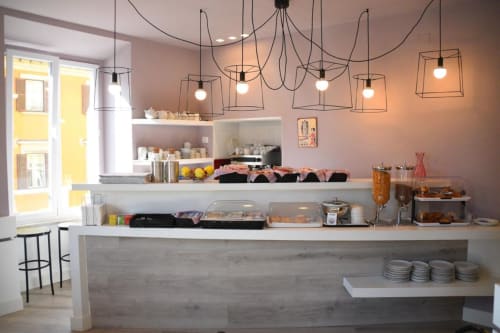 Modern pastry shop counter at Hotel Fiori Roma with geometric pendant lights, display cases, and baked goods