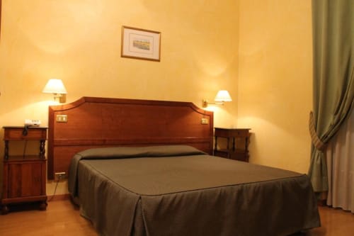 Elegante camera doppia presso l'Hotel Fiori Roma con testiera in legno, letti gemelli, pareti giallo caldo, lampade da comodino e parquet