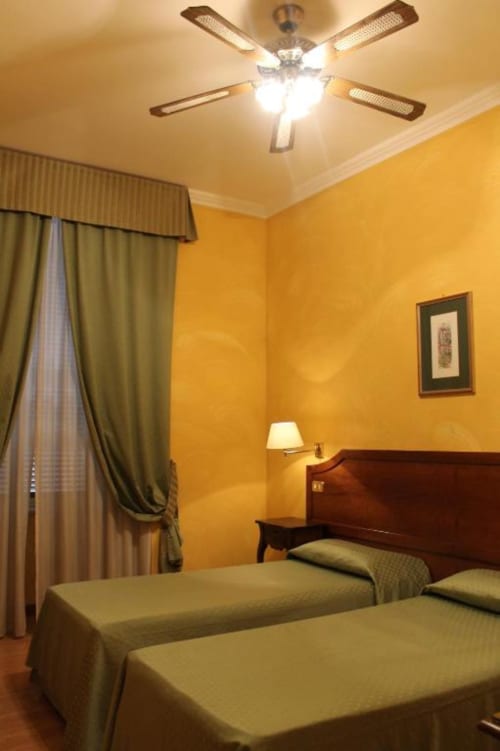 Camera doppia dell'Hotel Fiori Roma con due letti singoli, pareti gialle, ventilatore a soffitto e tende con vista sulla città