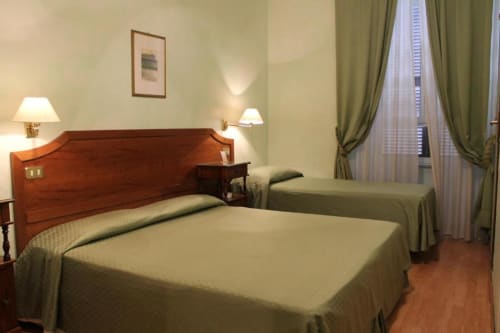 Camera tripla all'Hotel Fiori di Roma con due letti, testata in legno, lampade da comodino, tende verdi e vista sulla città