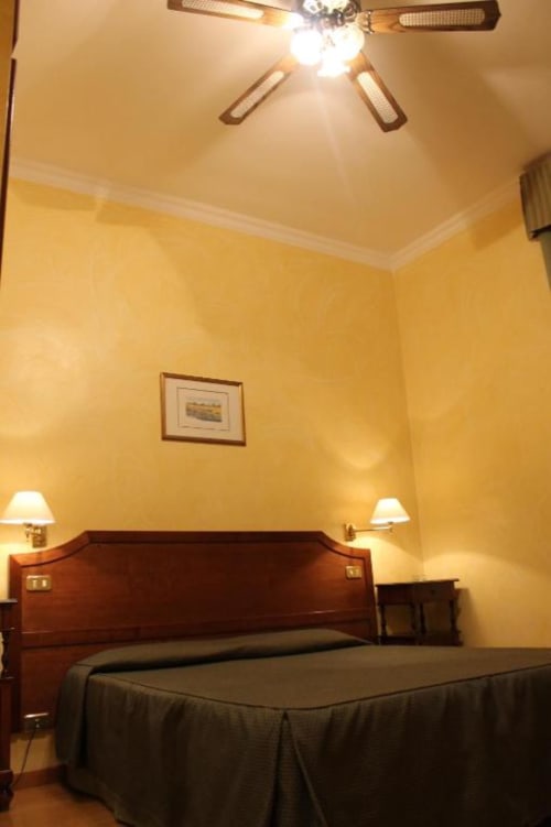 Camera dai toni gialli accoglienti all'Hotel Fiori Roma con letto in legno, letti gemelli, ventilatore a soffitto, lampade da parete e quadri incorniciati