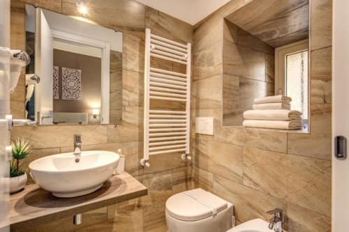 Bagno moderno di Chester Suites Roma con piastrelle in marmo, lavabo vessel, scaldasalviette e doccia effetto pioggia