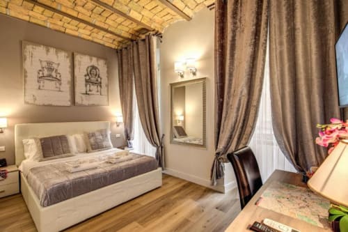 Elegante camera doppia al Chester Suites B&B di Roma con letto color crema, decorazioni artistiche, travi in legno e atmosfera calda