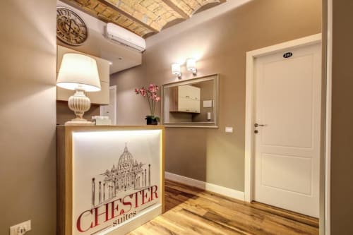 Banco reception di Chester Suites a Roma con elegante hall, orologio decorativo e orchidee rosa