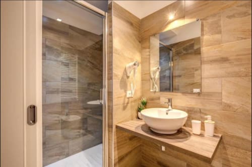 Moderno bagno presso Chester Suites Rome B&B con pareti in piastrelle di legno, lavabo rotondo bianco e doccia con box in vetro