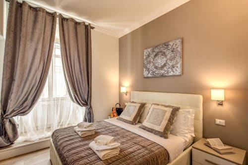 Camera elegante di Chester Suites Rome con testiera color crema, pareti tortora e tende stratificate