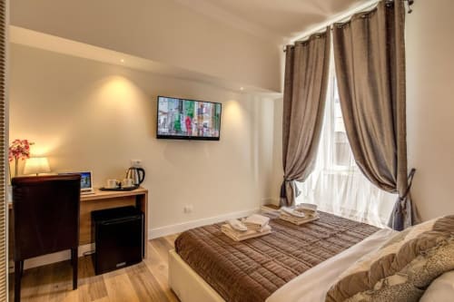 Camera da letto Chester Suites a Roma con letto matrimoniale, scrivania, TV e tende beige con vista sulla città