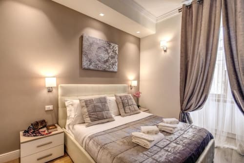Camera moderna presso Chester Suites B&B a Roma con letto color crema, biancheria grigia, applique murali e tende beige